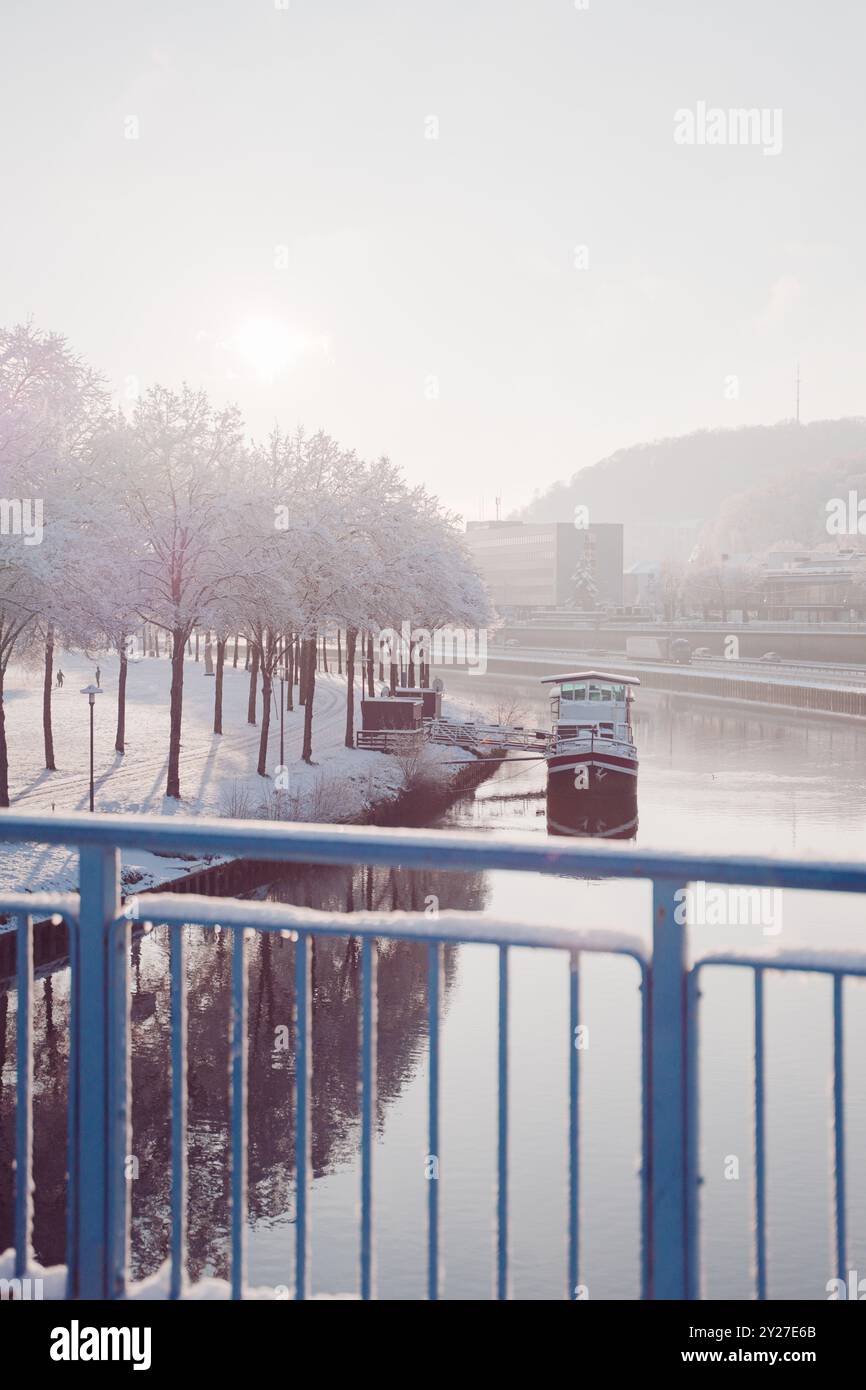 Rivière calme avec un bateau près d'une avenue de parc couverte de neige lors d'une journée d'hiver froide et brumeuse Banque D'Images