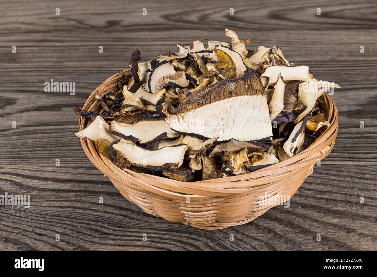 Gros plan de boletes séchées coupées en tranches dans un panier rond en osier sur fond de bois brun. Pile de champignons comestibles tranchés crus déshydratés dans un plat naturel. Banque D'Images