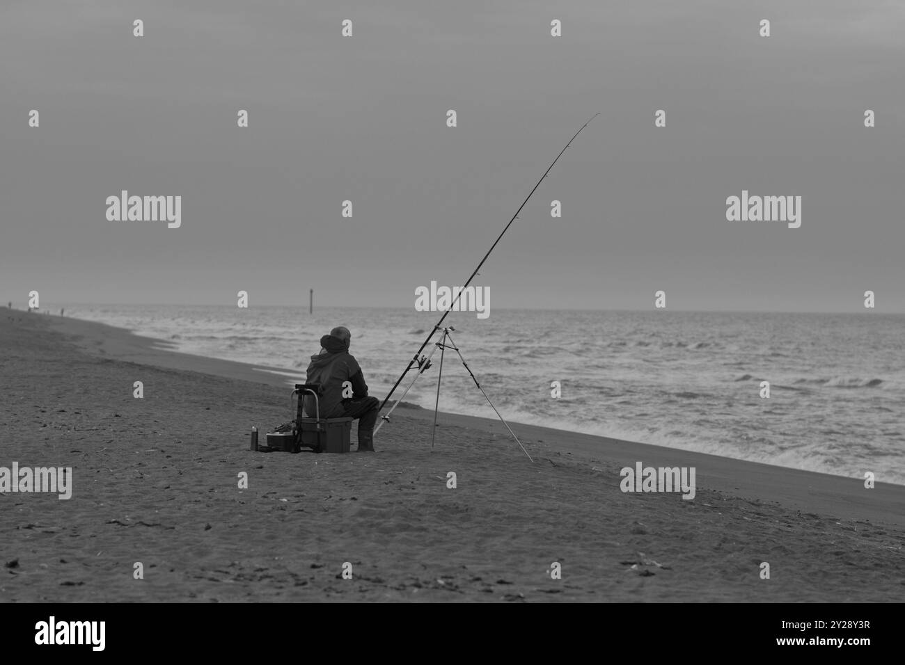 Un pêcheur de mer solitaire s'est assis sur la plage avec une canne à pêche attendant d'attraper une ligne de poisson capturé. Banque D'Images