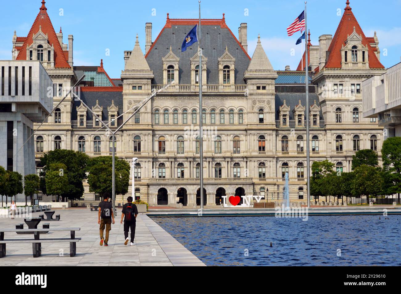 Les gens marchent devant le bâtiment du Capitole de l'État de New York à Albany, New York, à côté de l'Empire State Plaza reflétant la piscine Banque D'Images