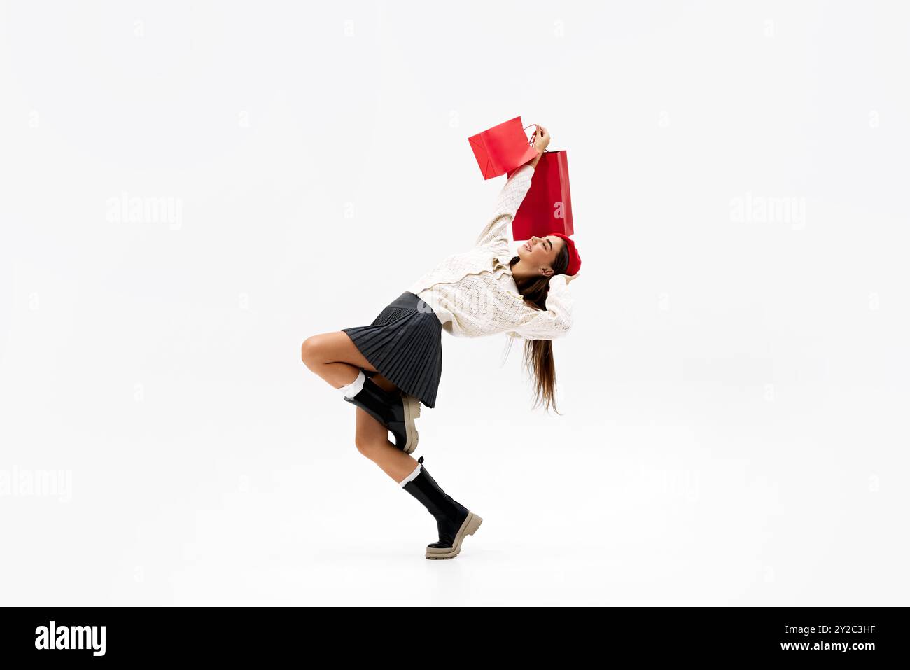 Jeune femme dans la pose dynamique, balançant de manière ludique ses sacs à provisions alors qu'elle exprime son bonheur sur fond blanc de studio. Banque D'Images