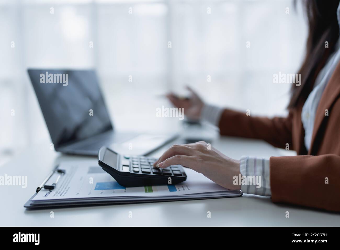 femme planifie méticuleusement un audit financier, en utilisant un ordinateur et une calculatrice pour examiner les documents budgétaires et s'assurer de l'exactitude. Banque D'Images