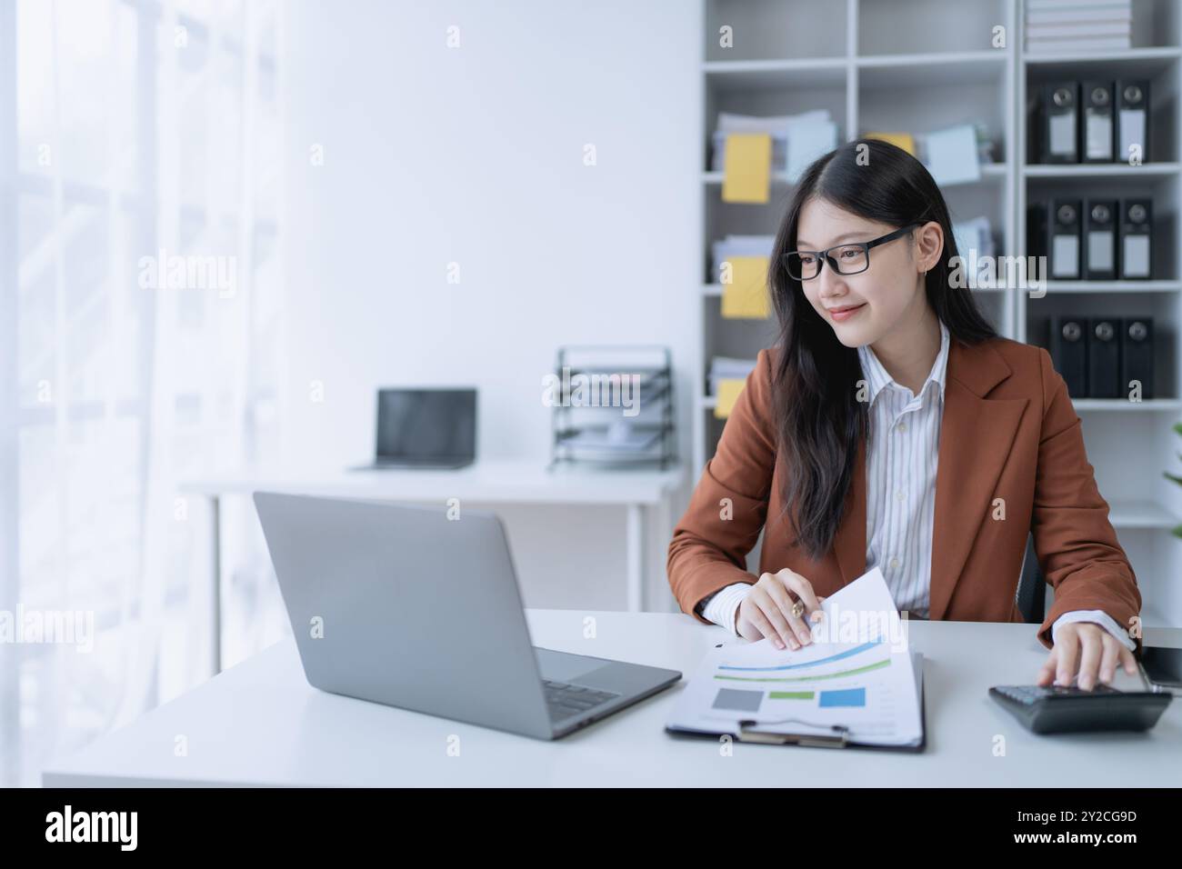 femme planifie méticuleusement un audit financier, en utilisant un ordinateur et une calculatrice pour examiner les documents budgétaires et s'assurer de l'exactitude. Banque D'Images