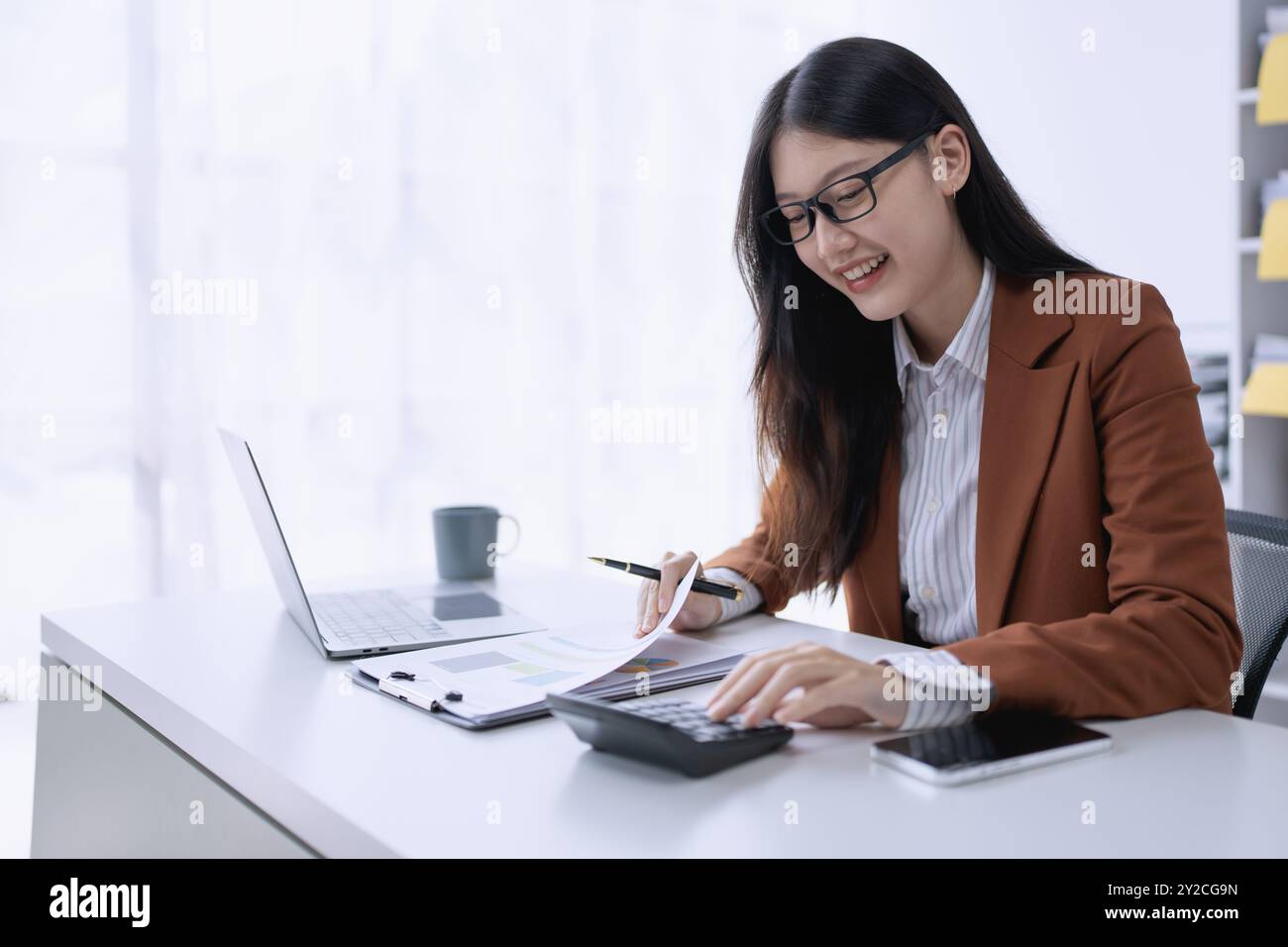 femme planifie méticuleusement un audit financier, en utilisant un ordinateur et une calculatrice pour examiner les documents budgétaires et s'assurer de l'exactitude. Banque D'Images