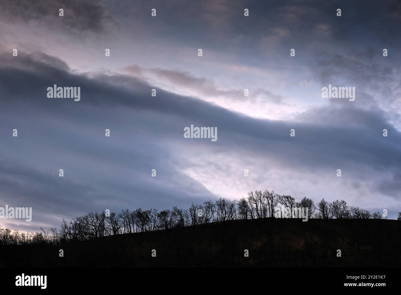 Des nuages sombres planent au-dessus d'une colline brûlée à Legarda, en Navarre, en Espagne, mettant en évidence les terribles conséquences d'un incendie de forêt. Banque D'Images