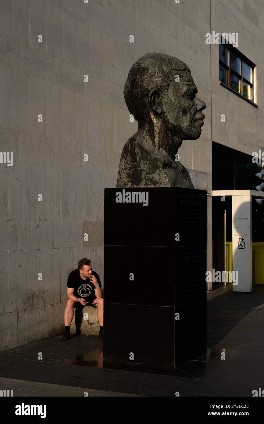 Un homme fumant une cigarette derrière le buste de Nelson Mandela devant le Royal Festival Hall, Southbank, Londres, Royaume-Uni. 5 juin 2024 Banque D'Images