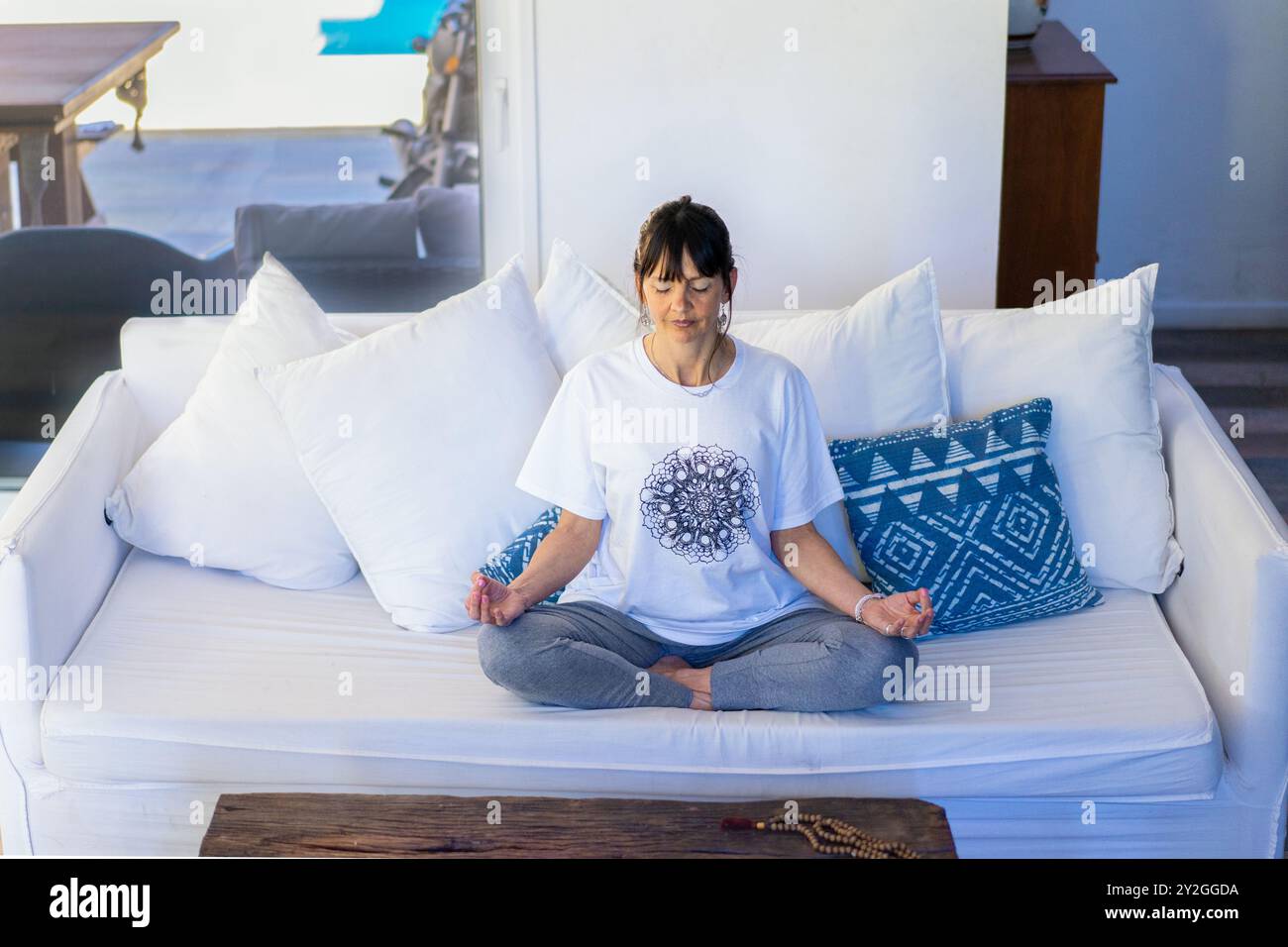 Vue en angle élevé d'une femme mi-adulte assise sur son canapé méditant à la maison, les mains dans Gyan Mudra, avec la frange et les cheveux tirés en arrière Banque D'Images