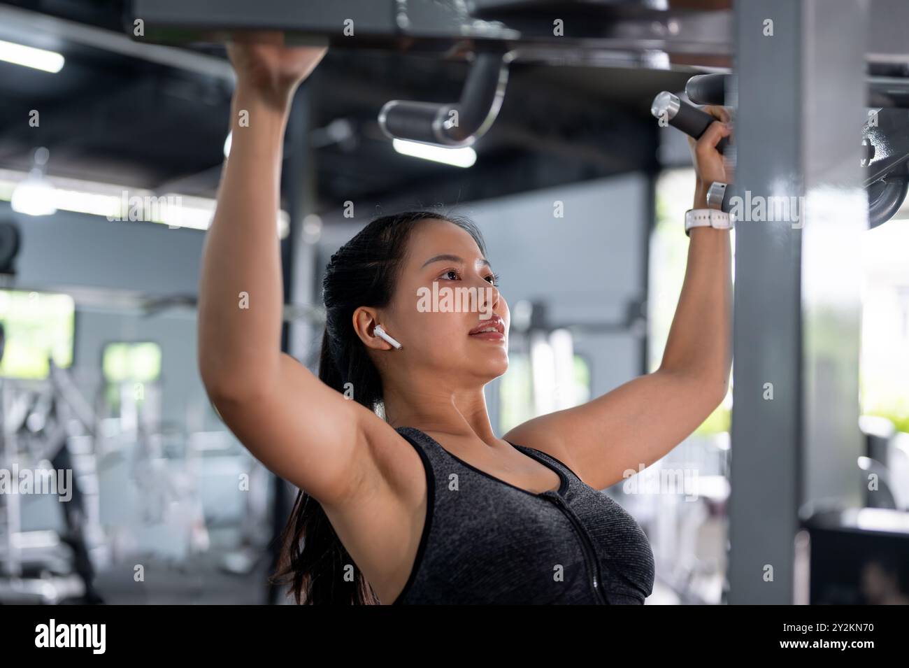Une image en gros plan d'une femme asiatique forte et sportive en vêtements de sport s'exerce aux barres de traction dans le gymnase, entraînant ses épaules et ses bras. entraînement, Banque D'Images