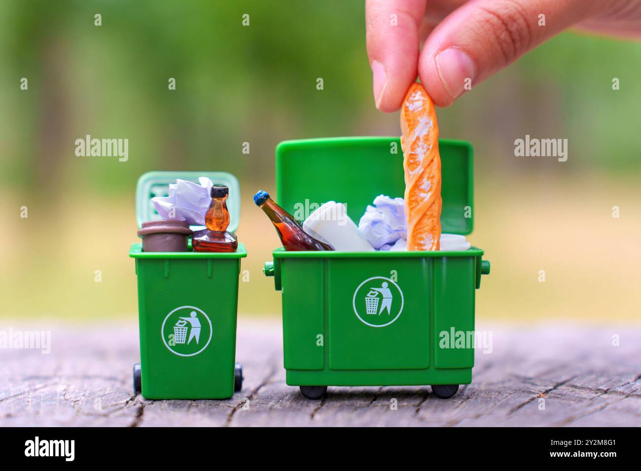 Placer à la main une baguette française dans une poubelle miniature verte, illustrant l'acte d'élimination des déchets et les efforts de recyclage. Banque D'Images