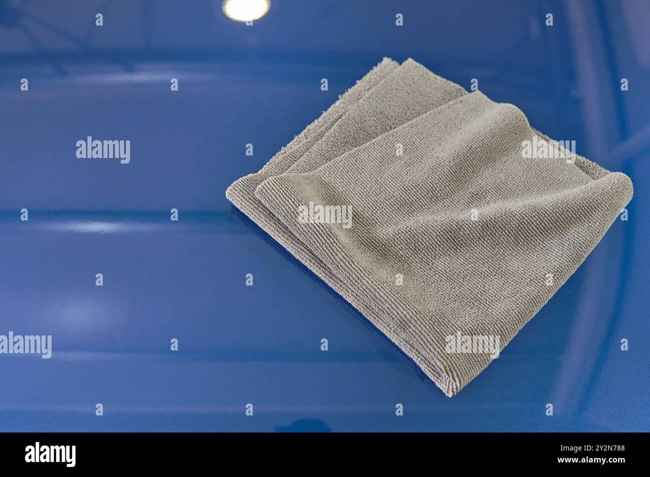 Le chiffon en microfibre de nettoyage de voiture de couleur grise est sur un capot de voiture propre Banque D'Images