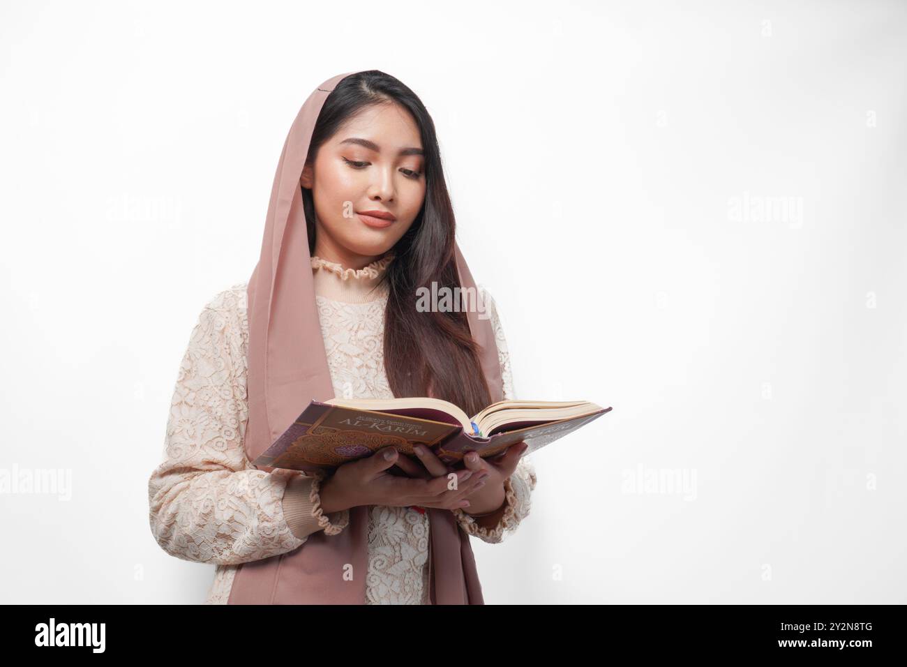 Femme musulmane asiatique sérieuse portant le voile hijab priant et lisant Al Coran, debout sur fond blanc isolé. Ramadan et Aïd Moubarak concept Banque D'Images