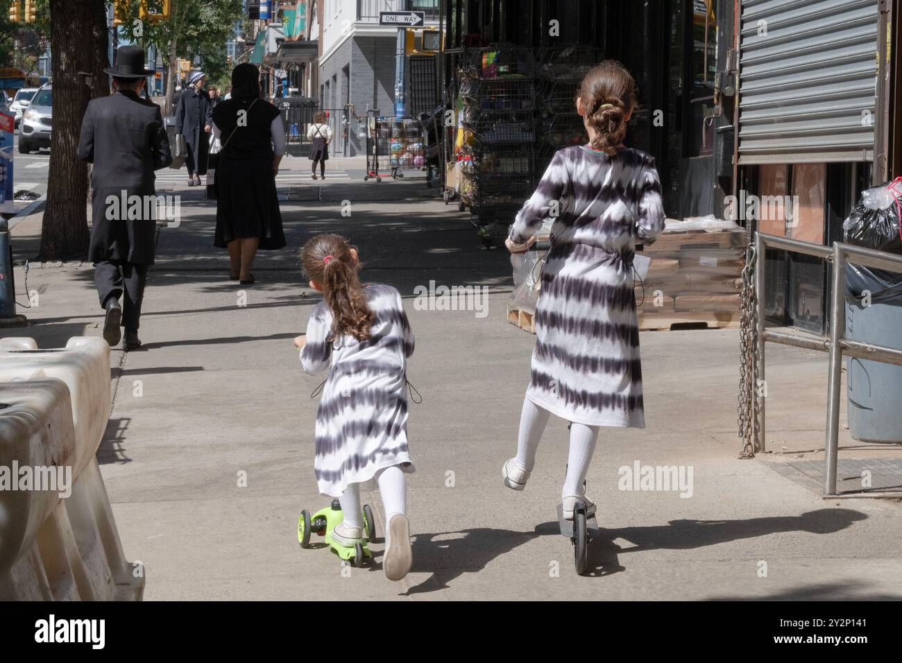 Deux sœurs à queue de poney vêtues à l'identique conduisent leurs scooters sur Lee Avenue à Williamsburg, Brooklyn, New York, un quartier juif hassidique. Banque D'Images