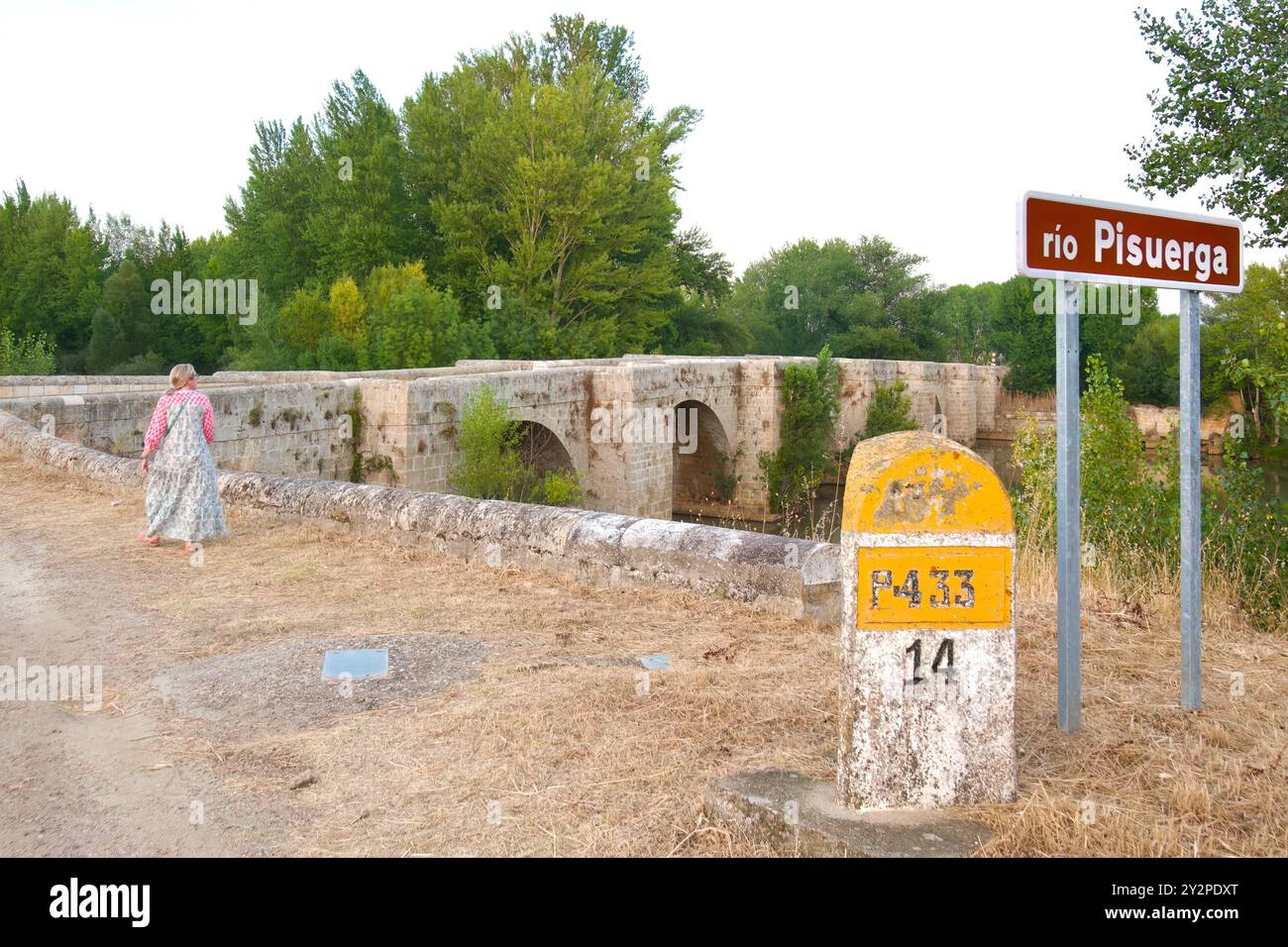 Femme dans une longue robe marchant vers le pont de la route romaine sur la rivière Pisuerga sur une chaude journée d'été avec une pierre de 14 km Lantadilla Palencia Espagne Banque D'Images