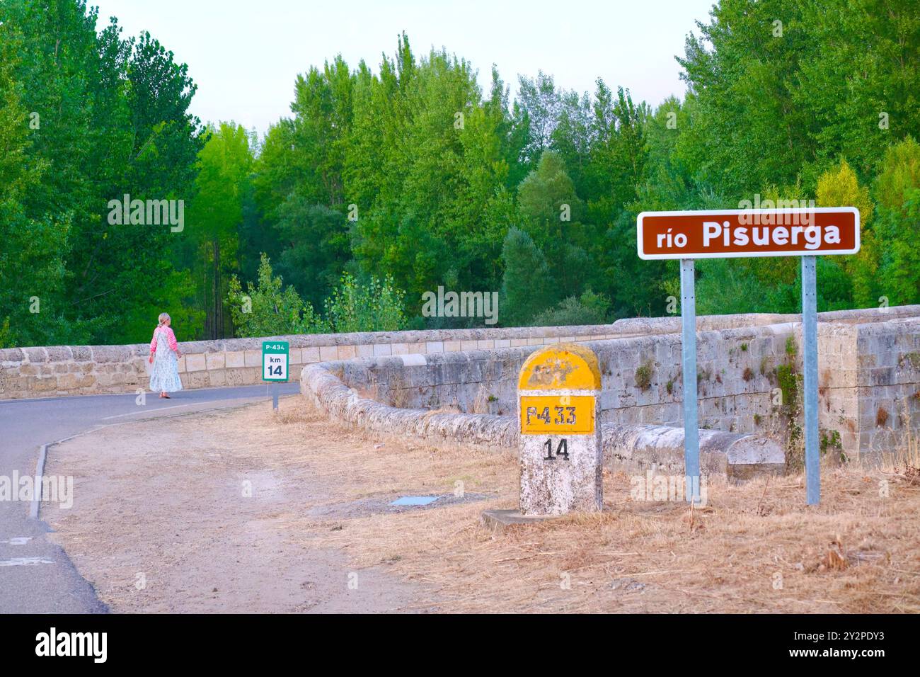 Femme dans une longue robe marchant vers le pont de la route romaine sur la rivière Pisuerga sur une chaude journée d'été avec une pierre de 14 km Lantadilla Palencia Espagne Banque D'Images