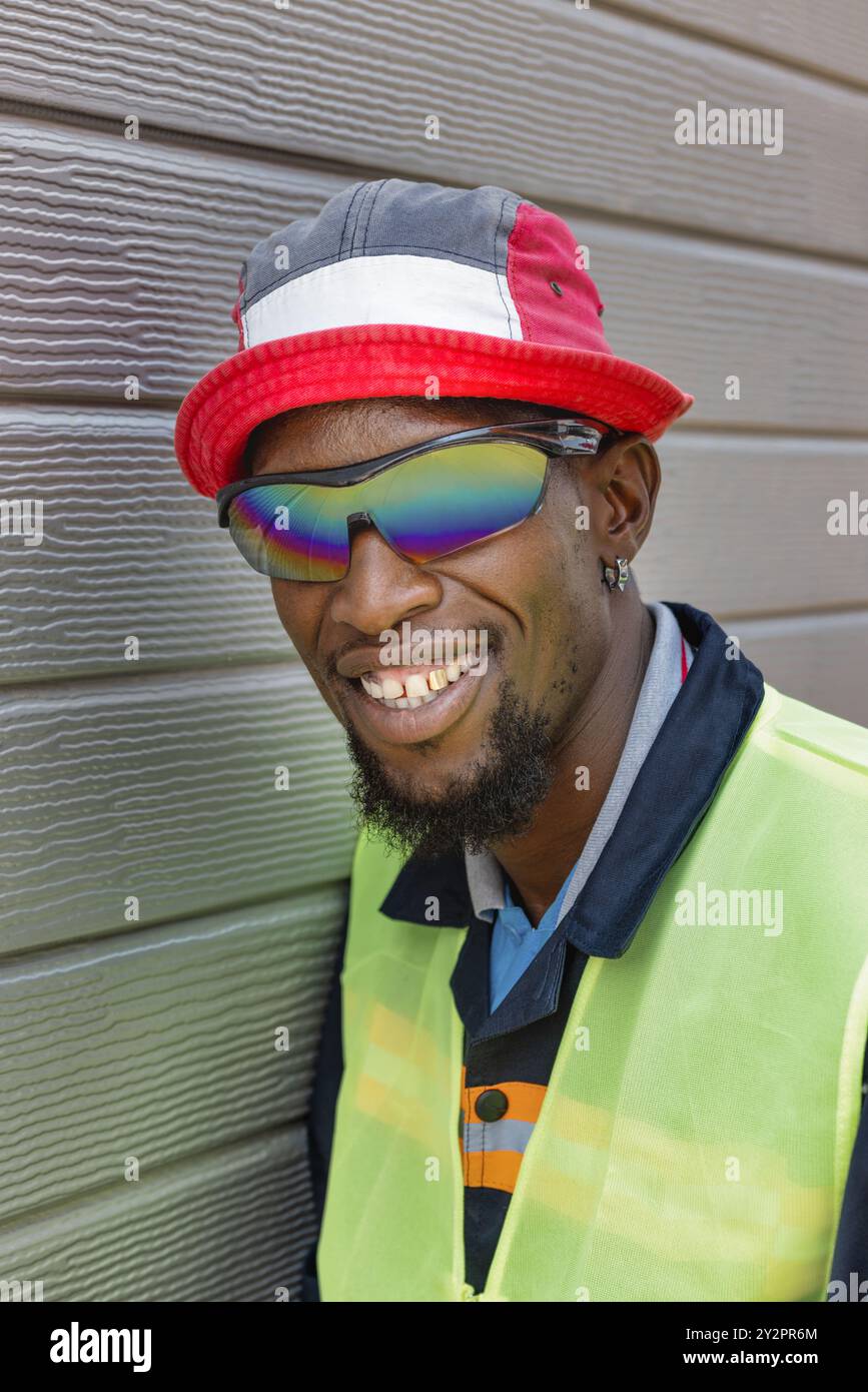 ouvrier africain avec un grand sourire et une dent d'or portant des lunettes de soleil et un chapeau Banque D'Images