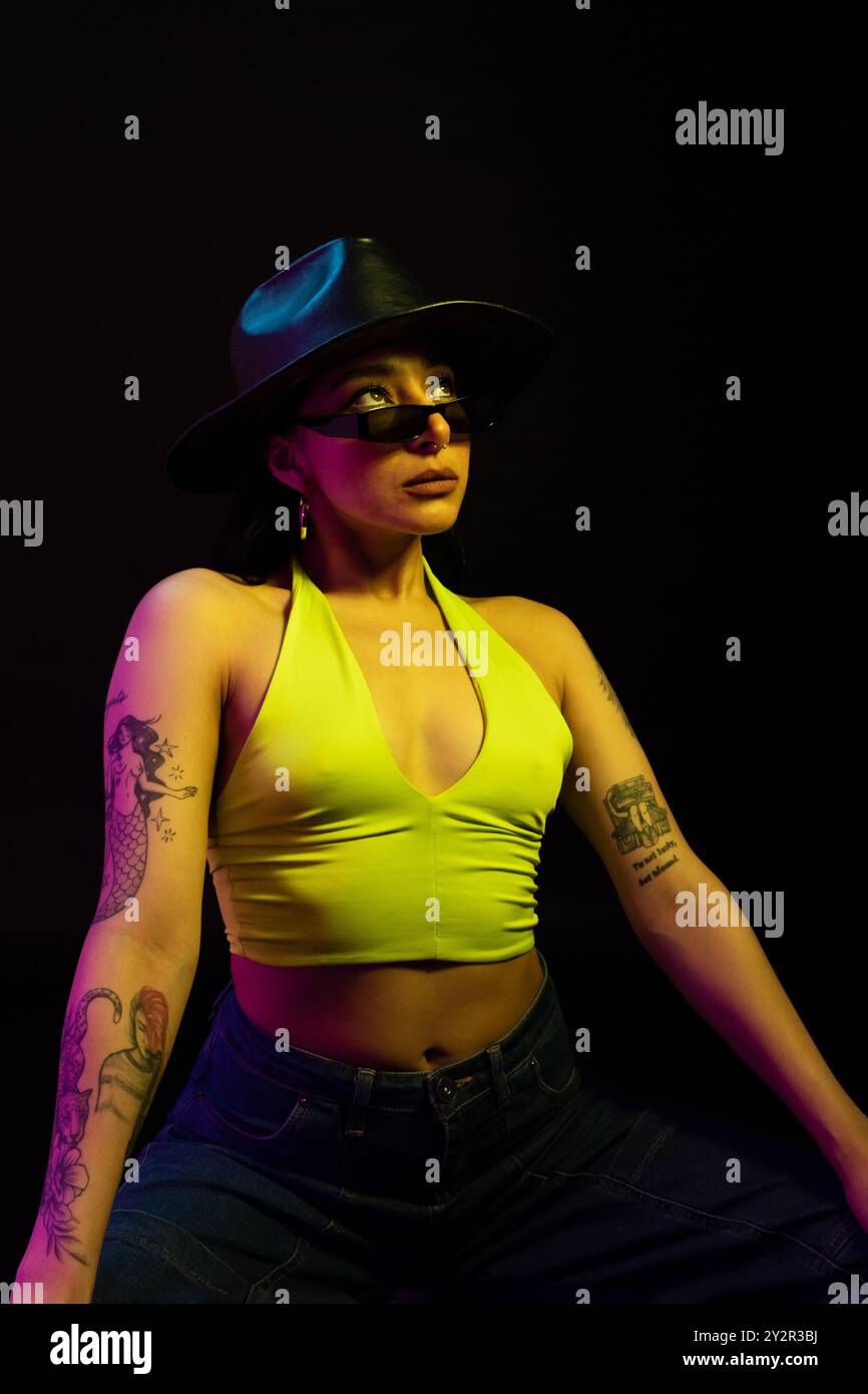 Une mannequin mexicaine regarde loin de l'appareil photo, portant un haut jaune fluo vibrant et un élégant chapeau noir. Elle est placée sur un fond sombre, haut Banque D'Images