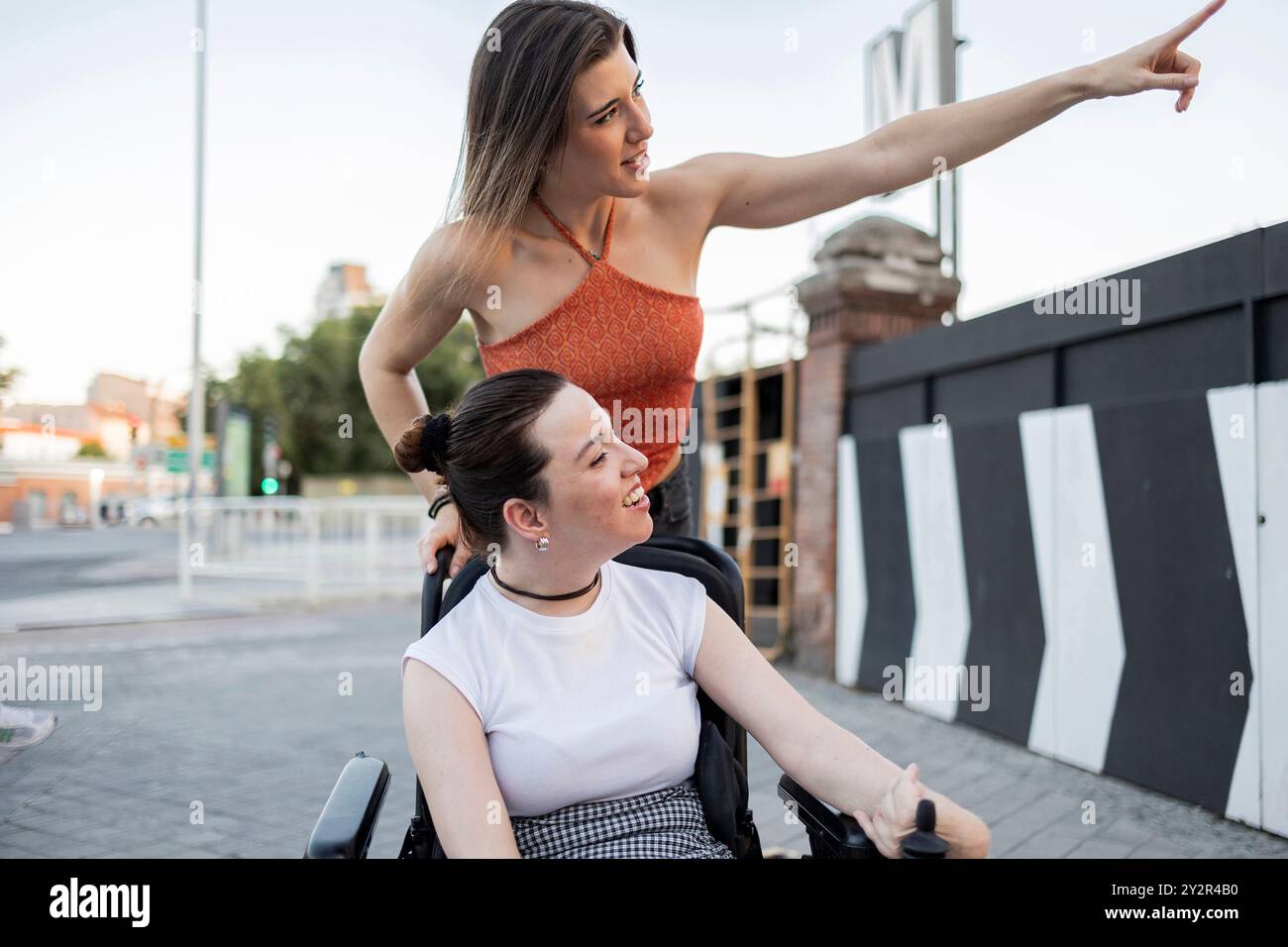 Un moment joyeux entre deux femmes, comme on souligne quelque chose d'intéressant à son amie en fauteuil roulant, ils sont à l'extérieur, exprimant le bonheur et c Banque D'Images