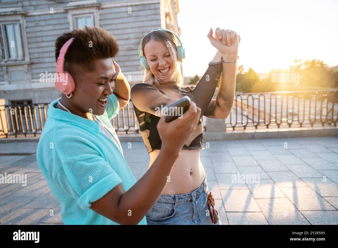 Deux heureux amis LGBTQIA+ dansent ensemble à l'extérieur, en profitant de la musique et d'un beau coucher de soleil. Ils partagent un moment de joie et d’amitié. Banque D'Images