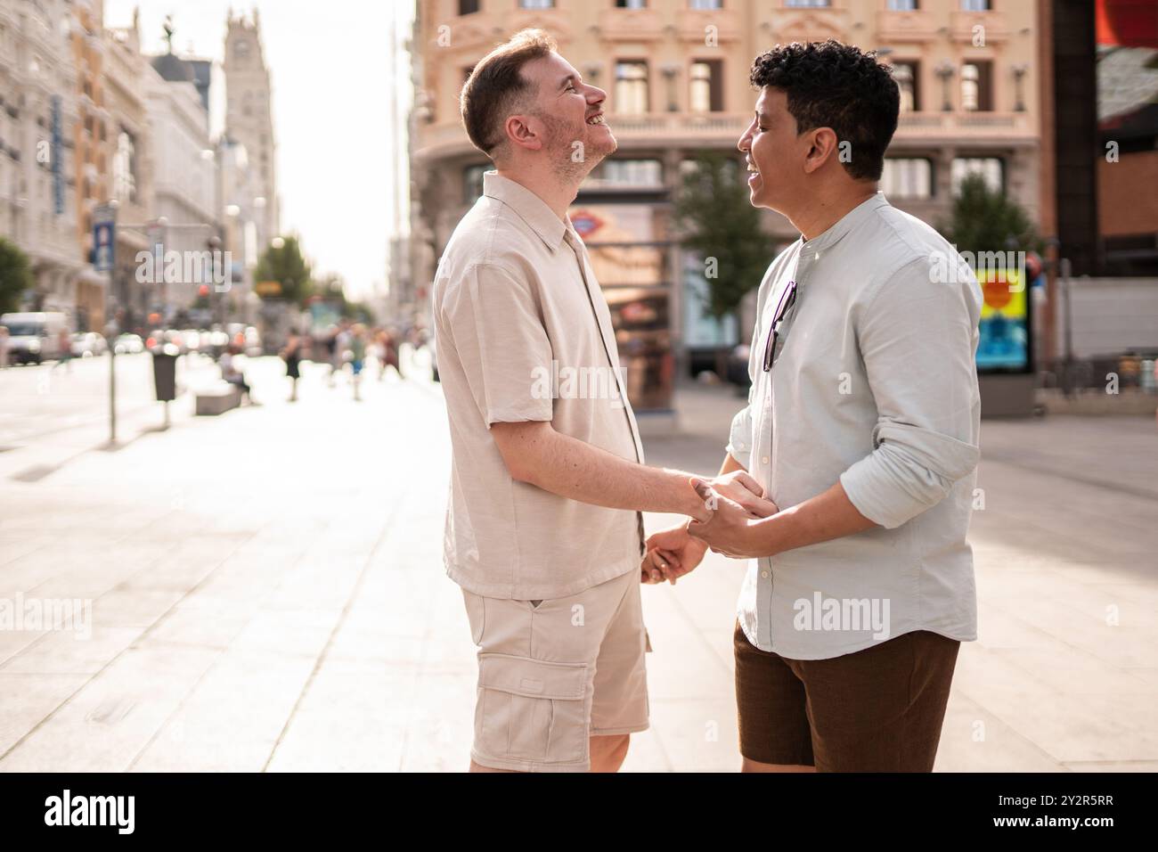 Un couple gay multiethnique partage un moment joyeux, se tenant la main et se souriant dans une rue de la ville, dépeignant l'amour et la connexion dans une ville Banque D'Images