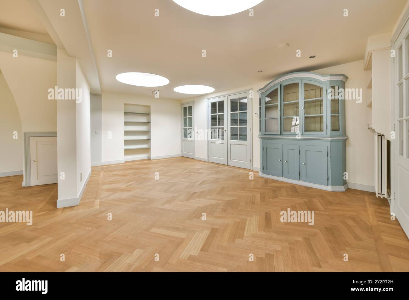 Cette chambre spacieuse et non meublée est dotée de parquet ciré à chevrons, de murs blancs avec un plafond lisse incurvé et d'armoires encastrées grises. Banque D'Images