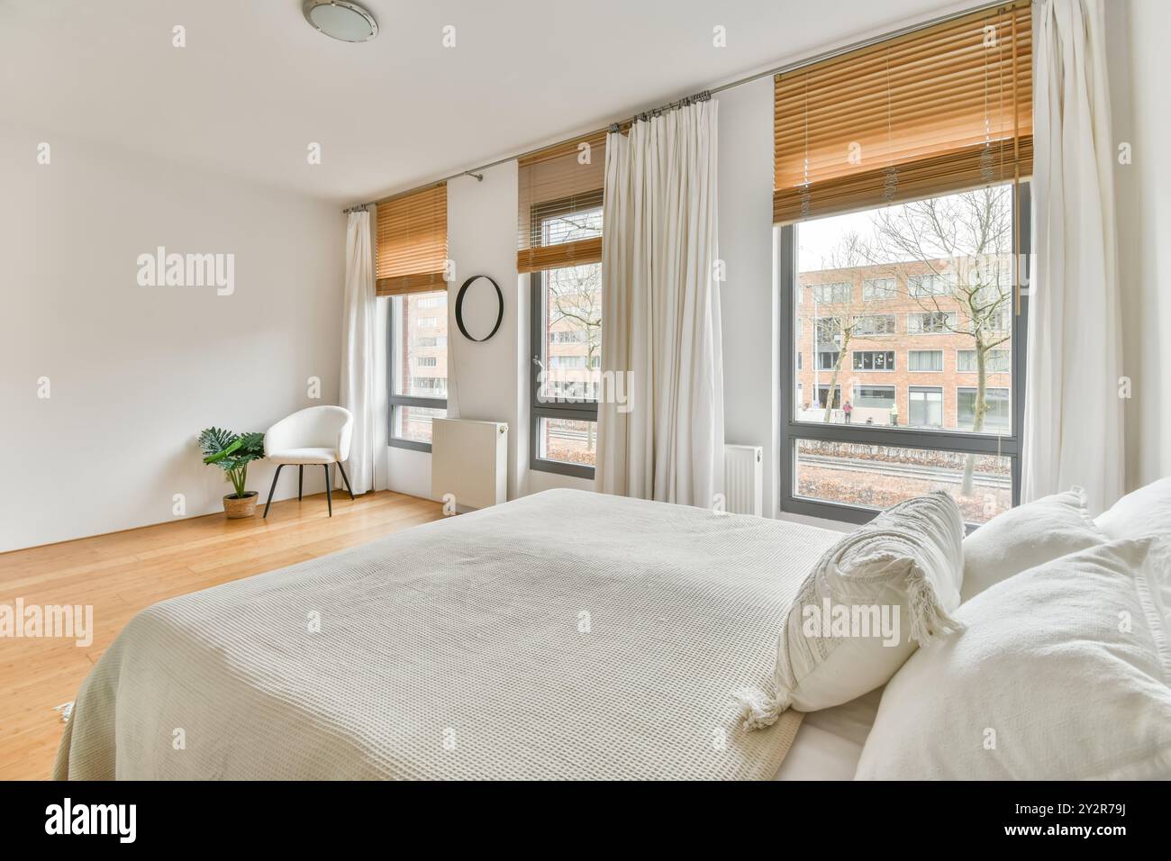 Cette chambre moderne lumineuse et aérée comprend de grandes fenêtres avec stores et un lit confortable. Banque D'Images