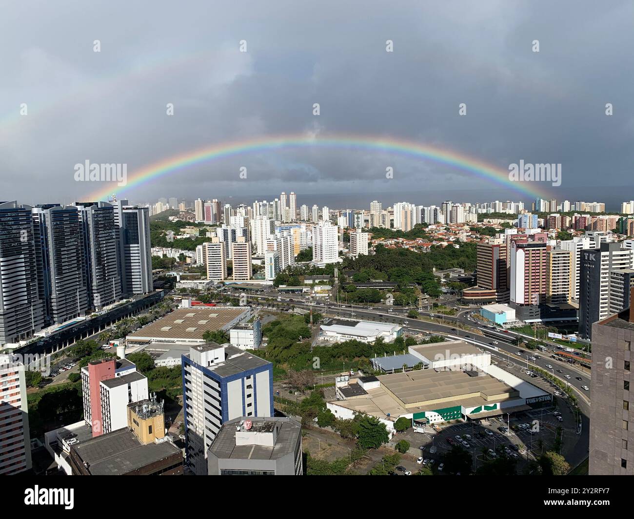 Une vue panoramique sur un paysage urbain avec un arc-en-ciel vibrant voûtant sur de hauts bâtiments et un mélange de zones résidentielles et commerciales. Banque D'Images