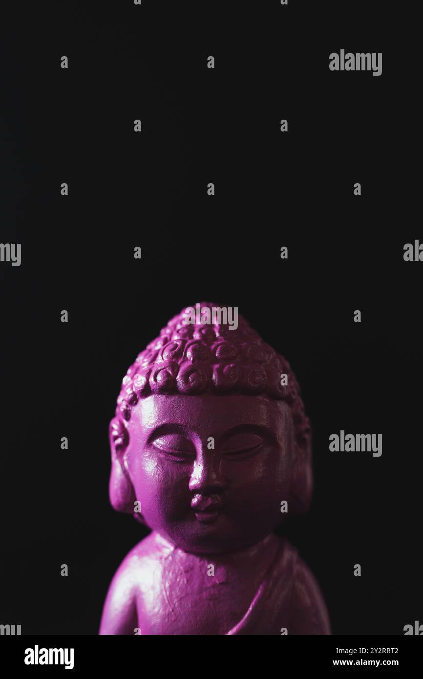 Une figure de Bouddha rose sur fond noir. Banque D'Images