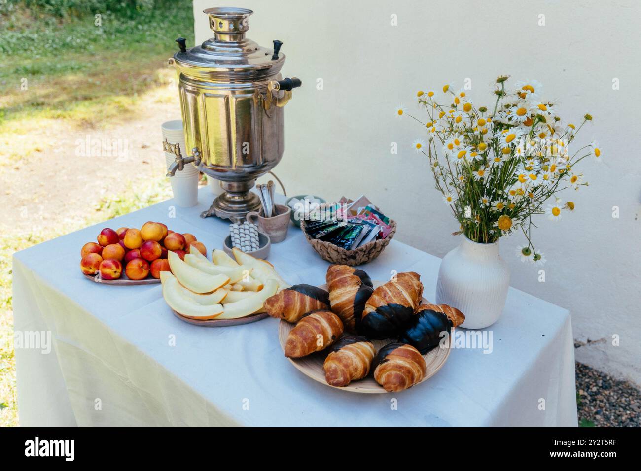 Un beau petit-déjeuner en plein air est préparé avec un samovar traditionnel, des croissants et des viennoiseries affichés sur une table, aux côtés de fruits frais et d'un vase Banque D'Images