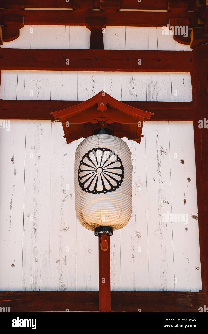 Lanterne traditionnelle japonaise en papier avec un emblème de chrysanthème accroché à une structure en bois dans un temple historique. Banque D'Images