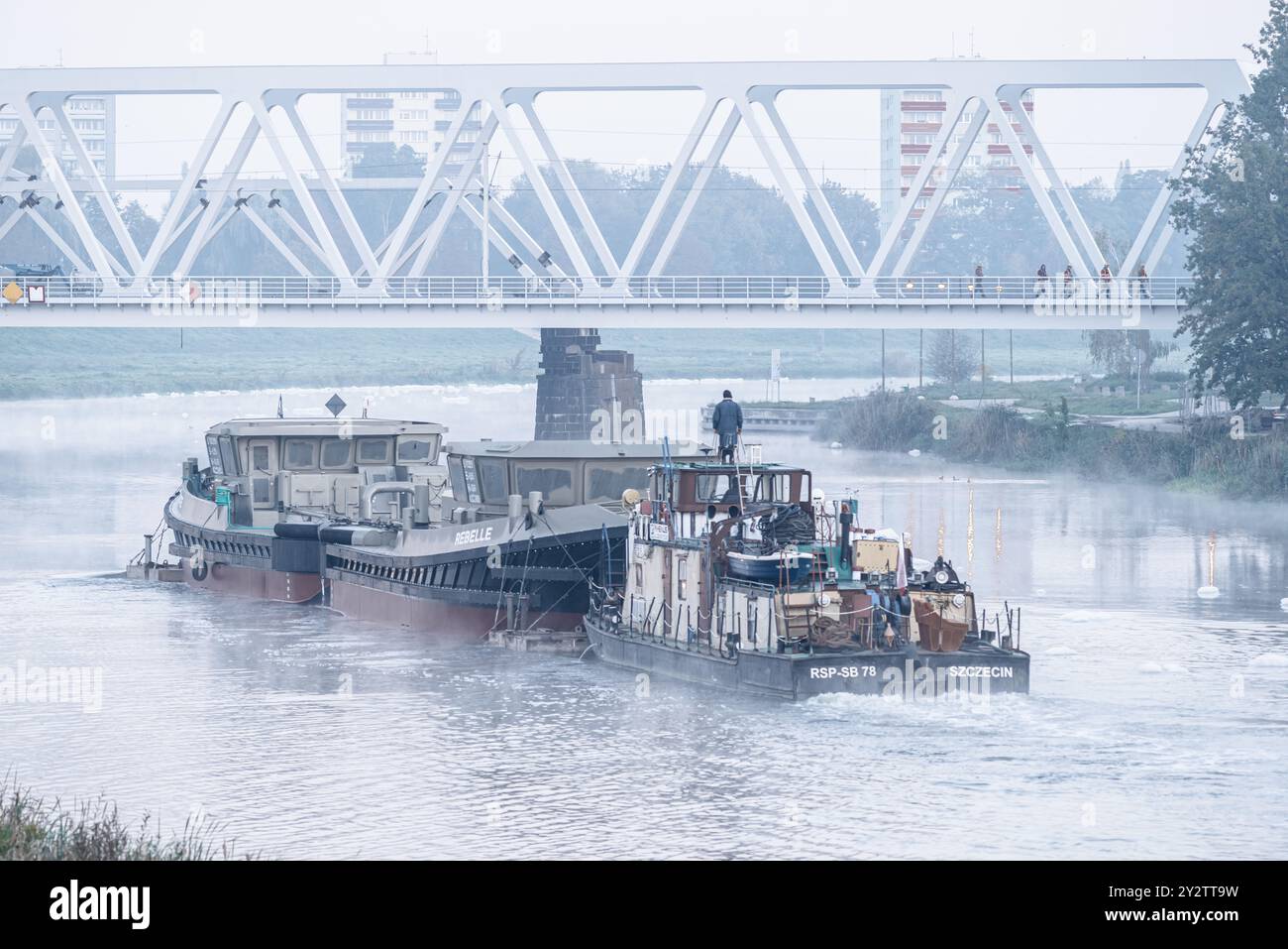 Une vue matinale brumeuse de deux remorqueurs sur une rivière avec un pont et des bâtiments de la ville en arrière-plan. Banque D'Images