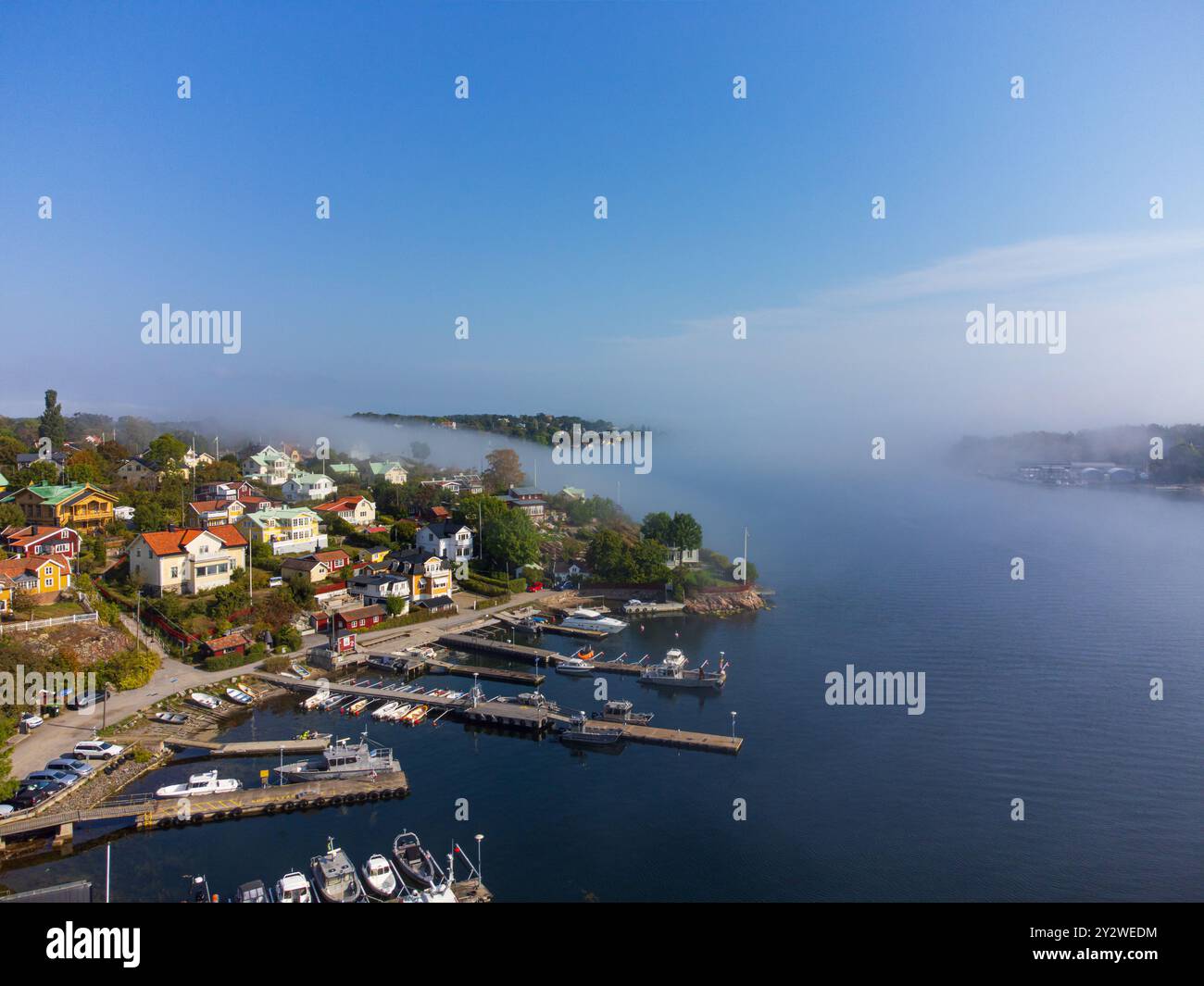 Brouillard matinal roulant sur une île au début de l'automne, Dalarö, archipel suédois, Suède. Maisons, arbres, bateaux. Ciel bleu, lumière du soleil éclatante Banque D'Images