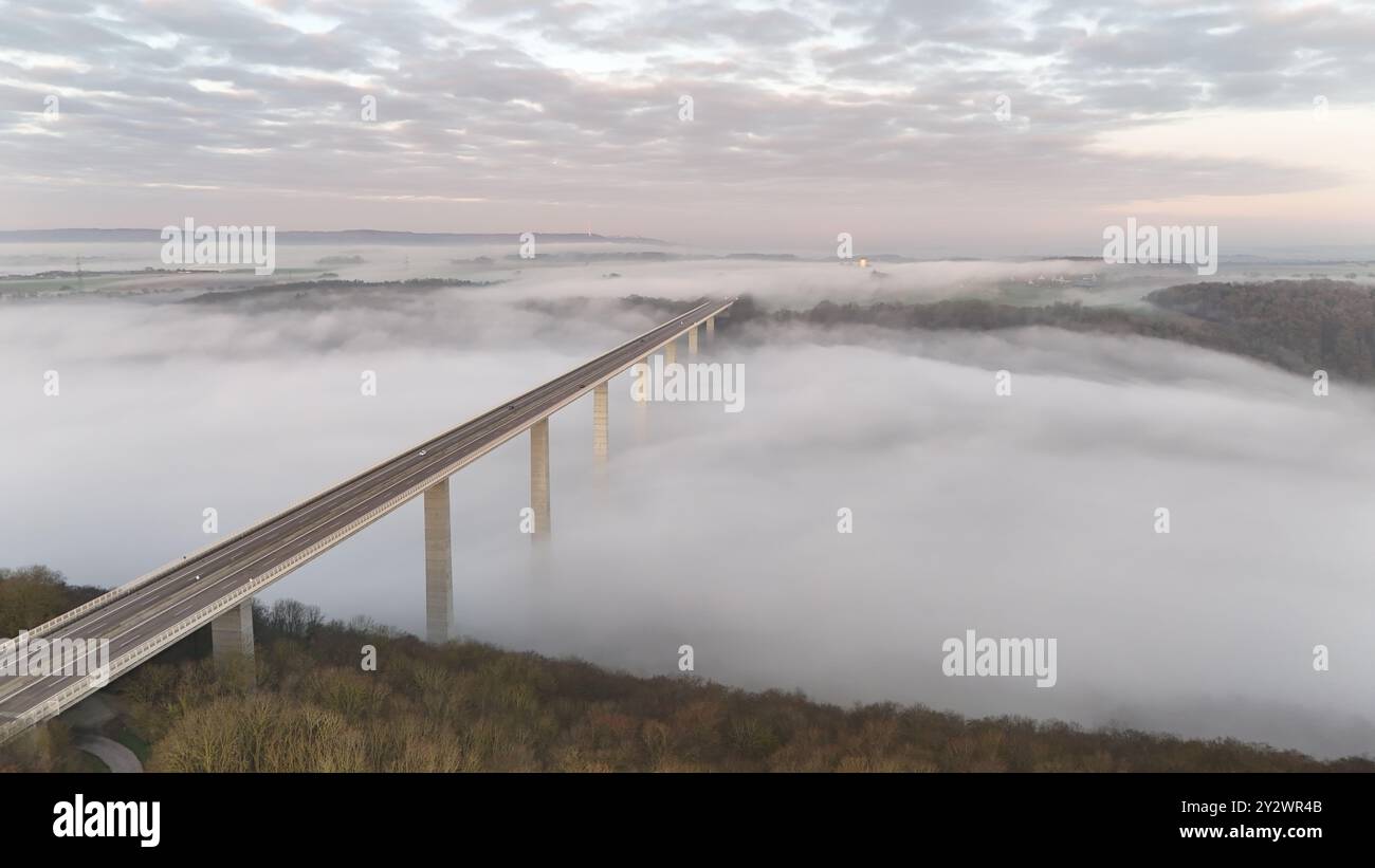 Une vue aérienne époustouflante d'un pont s'étendant sur un paysage brumeux avec un ciel nuageux Banque D'Images