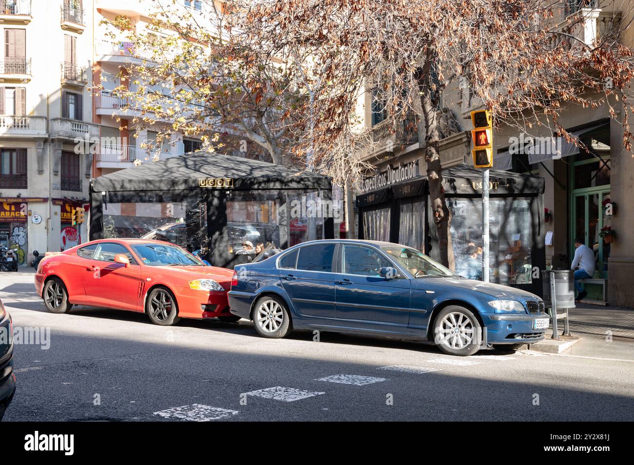 Détail d'un coupé Hyundai rouge à l'avant est un coupé BMW E46 bleu. Les deux voitures sont mal garées dans un coin de la ville de Barcelone devant un bar Banque D'Images