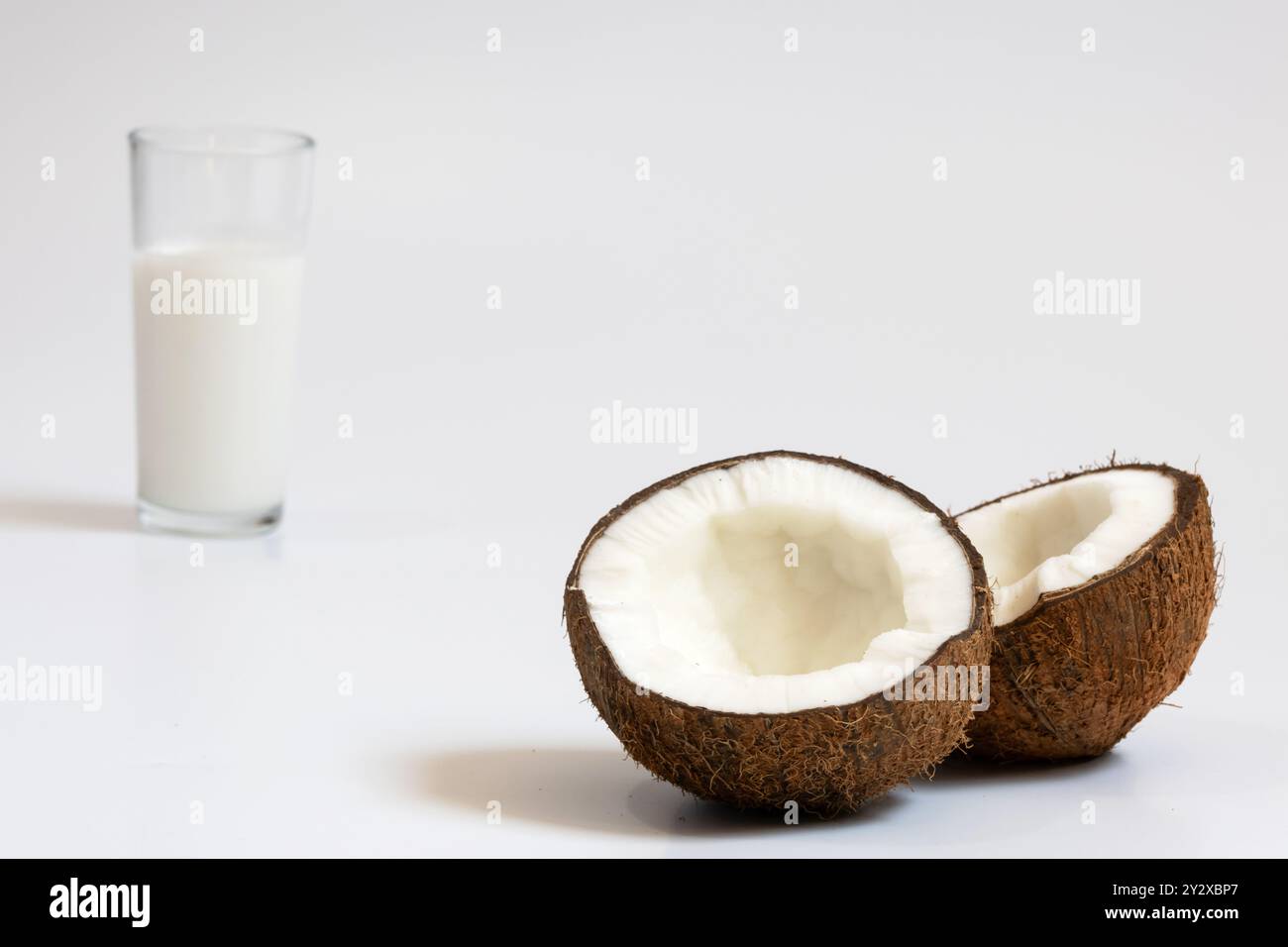 Deux parties d'une noix de coco mûre avec une pulpe très épaisse au premier plan, et un verre avec du lait de coco en arrière-plan et hors foyer. Banque D'Images