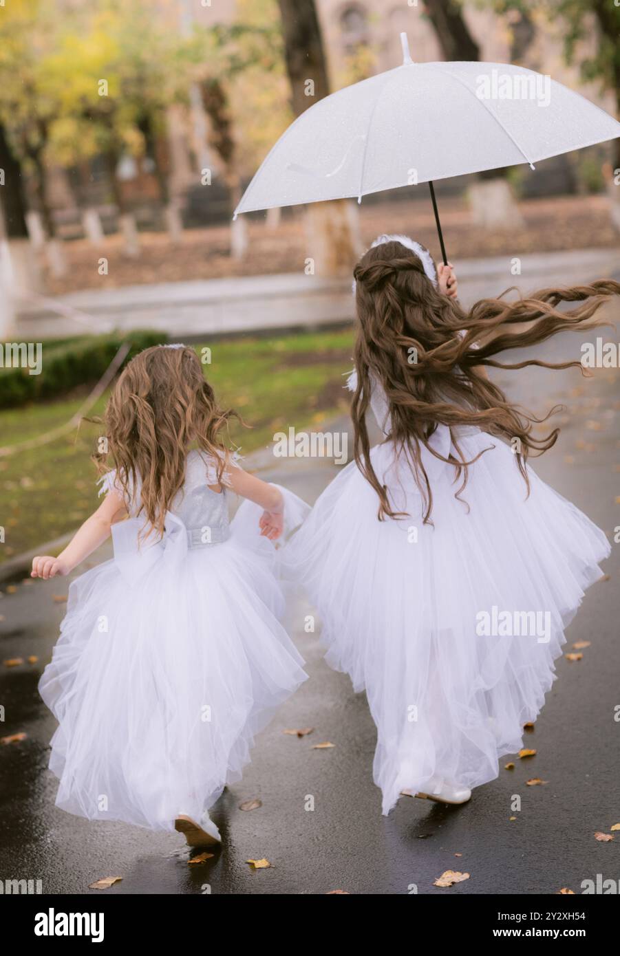 Une photo de fond de deux filles en longues robes de célébration blanches courant le long d'une rue avec parapluie Banque D'Images