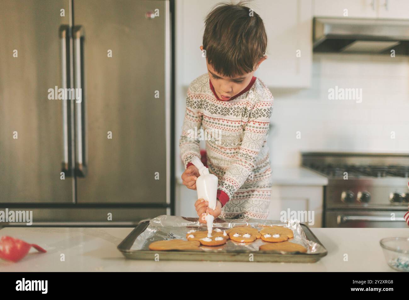 Un petit garçon décorant des biscuits de Noël en pyjama. Banque D'Images