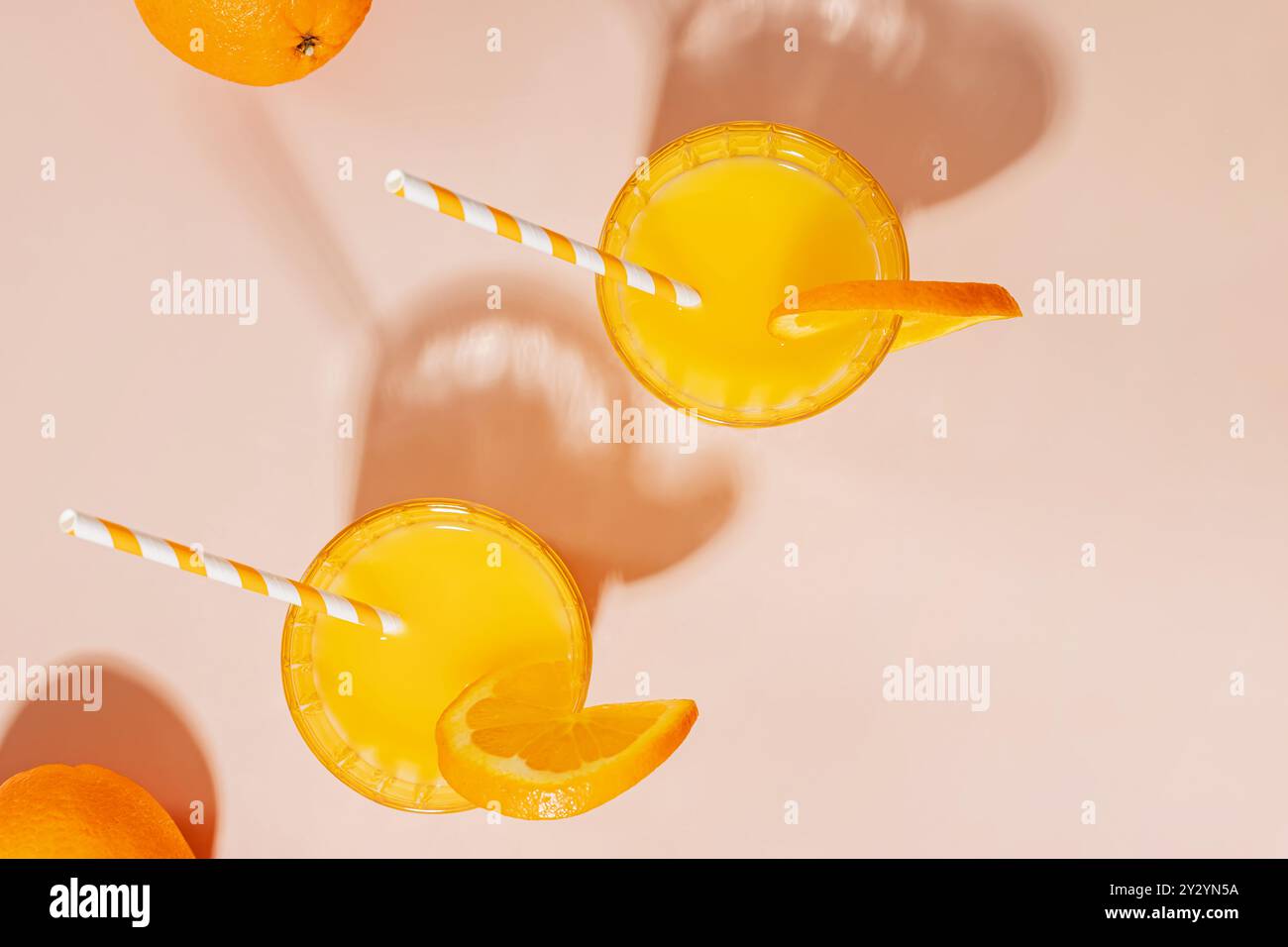 Deux verres de jus d'orange avec des pailles et des tranches d'orange sur un fond rose avec de longues ombres, boisson d'été Banque D'Images