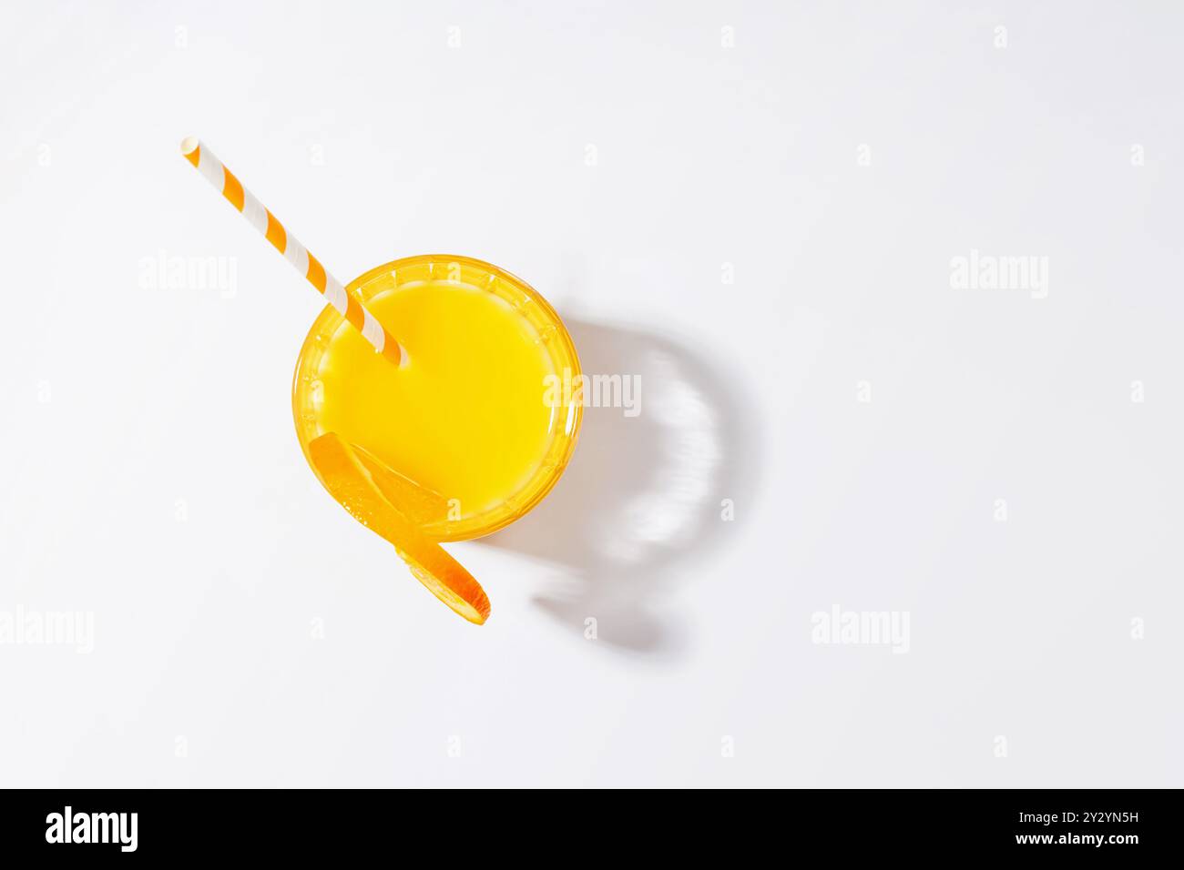 Jus d'orange dans un verre avec une paille sur un fond blanc, créant une ambiance rafraîchissante Banque D'Images