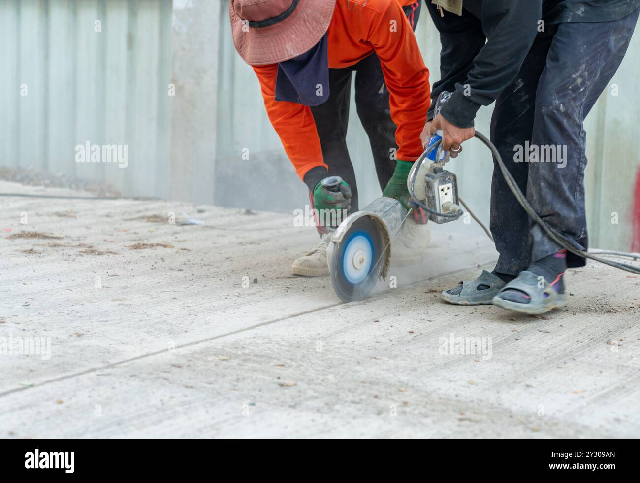 Les ouvriers de la construction utilisent une lame de scie circulaire coupant le trottoir en béton dans le site routier. Banque D'Images