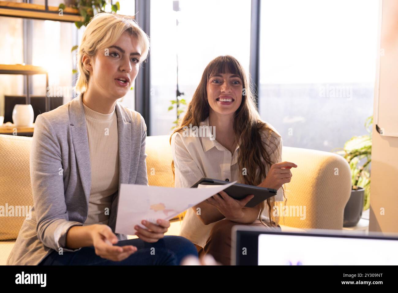 Au bureau, tenant des documents et une tablette, deux femmes discutent des idées créatives d'entreprise d'écriture Banque D'Images