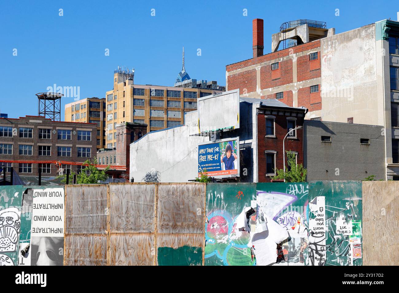 Un mélange de vieux loft industriels à Philadelphie, Pennsylvanie avec une clôture de construction en contreplaqué altéré au premier plan. Banque D'Images