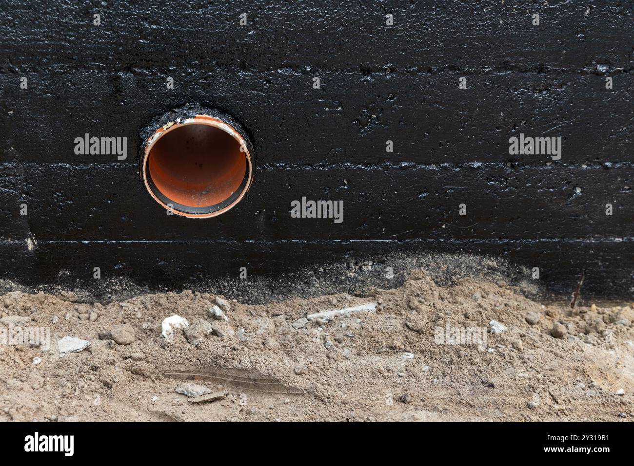 Le tube de drainage est monté dans le mur de fondation en bande en béton armé recouvert d'une composition de bitume noir de protection, vue de face Banque D'Images