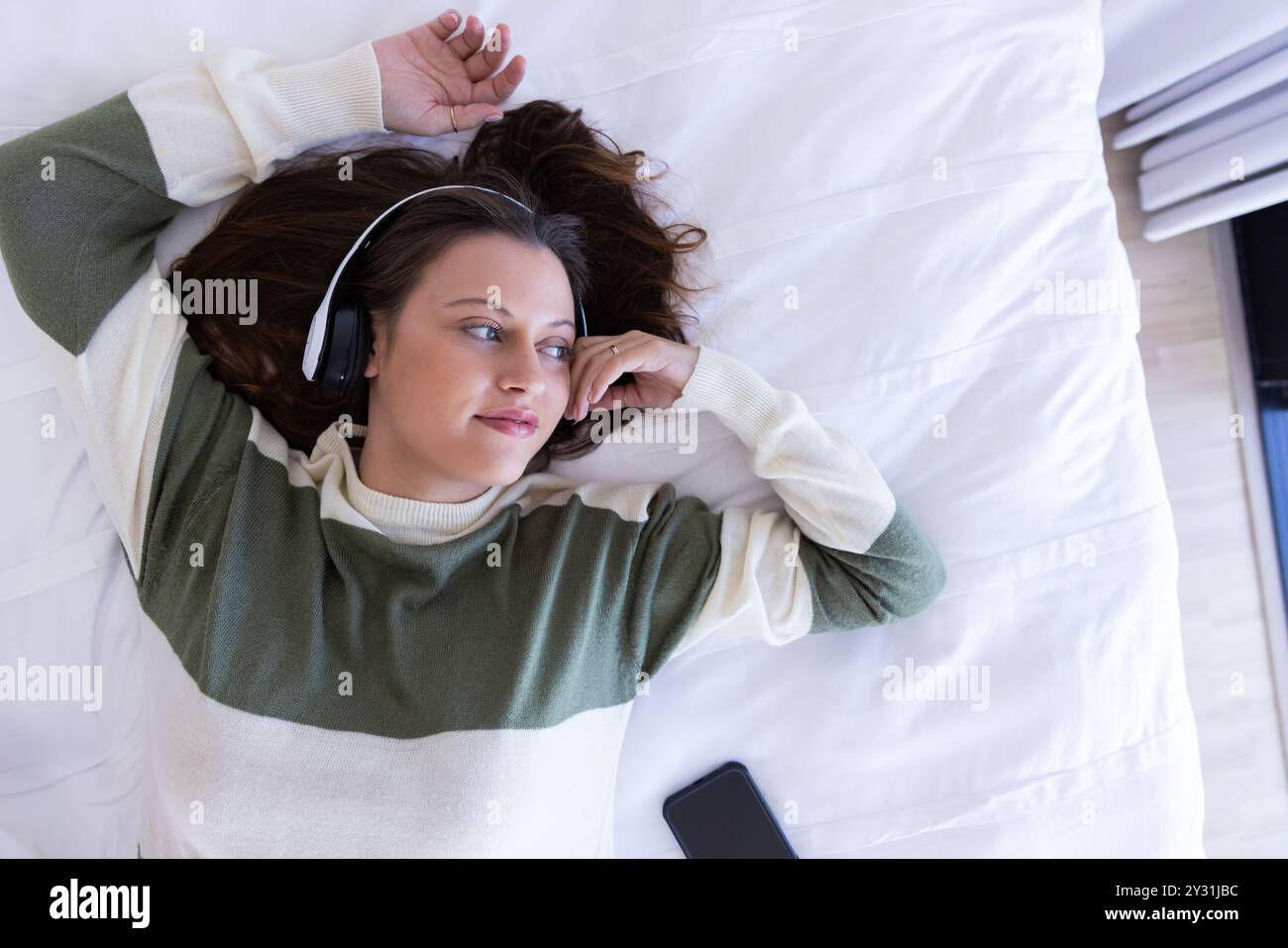 A la maison, écouter de la musique avec des écouteurs, femme se relaxant sur le lit avec smartphone à proximité Banque D'Images