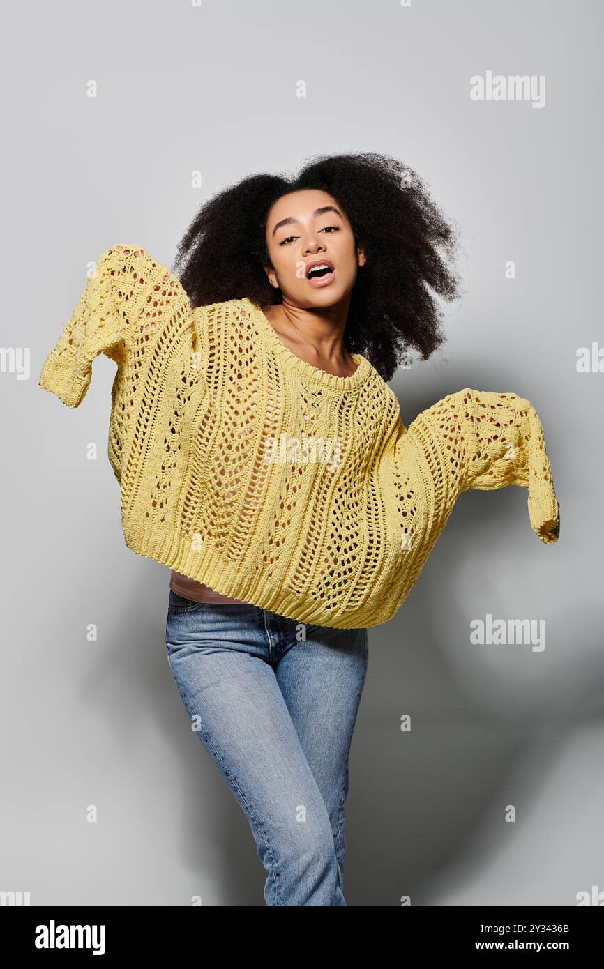 Une jeune femme aux cheveux bouclés met en valeur son esprit ludique tout en portant un pull jaune. Banque D'Images