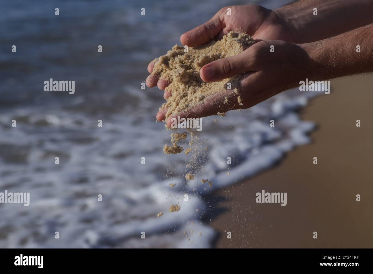 Gros plan des mains d'un homme blanc bronzé ramassant du sable de la plage et le laissant tomber au coucher du soleil. Banque D'Images