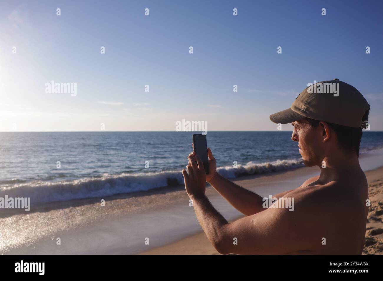 concentré jeune garçon accordé au coucher du soleil sur la plage déserte prenant une photo avec son téléphone portable Banque D'Images