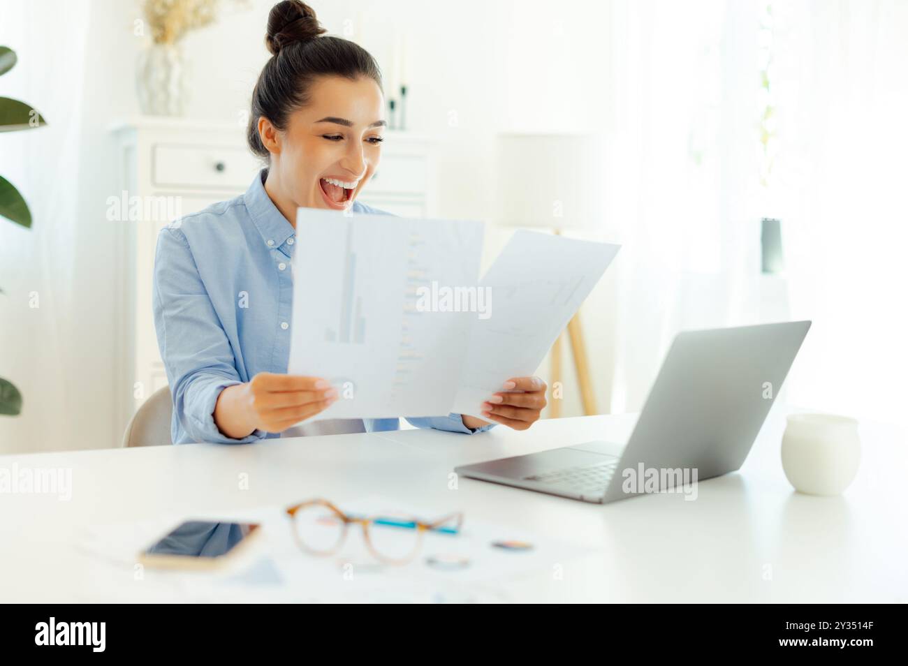 Heureuse joyeuse femme d'affaires indienne ou arabe réussie assise sur un lieu de travail, analysant des documents financiers, se réjouissant du succès, de bons résultats de travail, souriant Banque D'Images