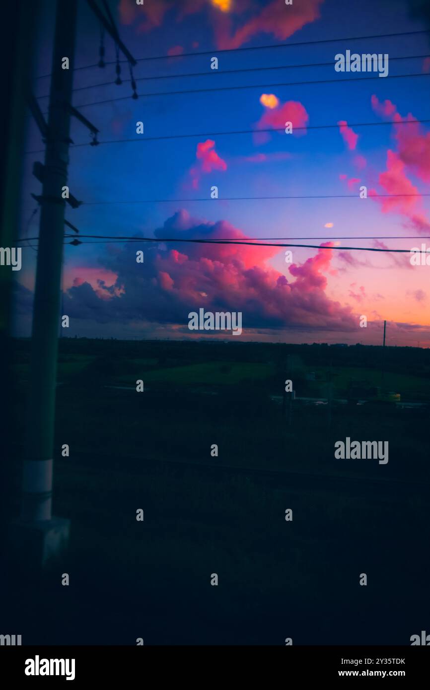 De la fenêtre du train en mouvement, un beau paysage se déploie dans la lumière de fin de soirée. Le soleil se couche, projetant différentes couleurs sur le clou Banque D'Images