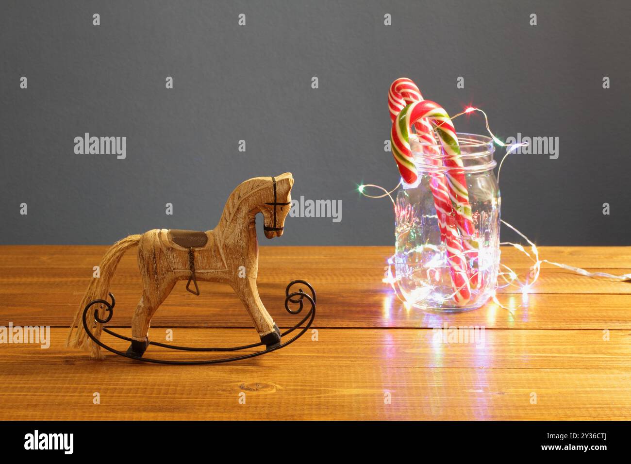 Décoration de Noël - petit cheval à bascule en bois et bonbons du nouvel an au caramel dans un pot en verre, agrémenté d'une guirlande lumineuse festive sur un tabl Banque D'Images