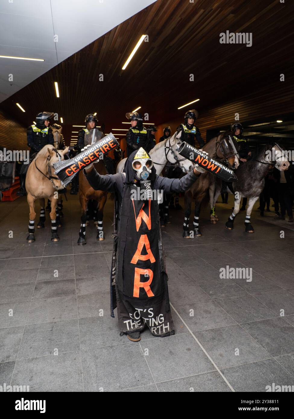 Un manifestant en costume tient un support de missile cassé lisant : « CESSEZ-LE-FEU MAINTENANT ! » Devant une ligne de chevaux de la police, Un blocus planifié et une manifestation contre les Forces terrestres 2024, la plus grande exposition de l'industrie de la défense dans l'hémisphère sud, ont éclaté en affrontements avec la police tout au long de la journée. Les manifestants tentant d'empêcher l'entrée de la convention ont jeté des objets et des liquides sur les policiers, construit de petits barrages et déclenché des incendies de poubelles, tandis que la police a utilisé la force, le gaz poivre, les gaz lacrymogènes, les grenades paralysantes et les balles en caoutchouc sur les manifestants (photo Alex Zucco/SOPA images/Sipa USA) Banque D'Images